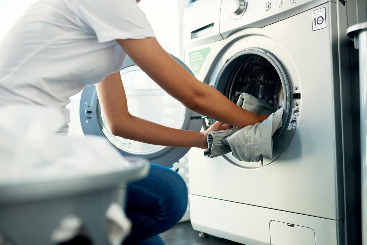 Kvinna lägger kläder i tvättmaskin