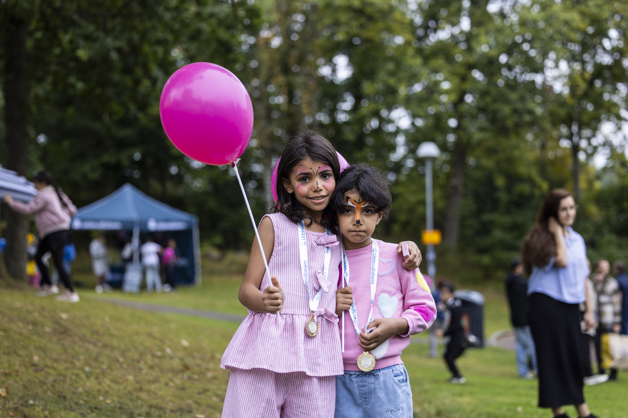 Två ansiktsmålade flickor med rosa kläder och rosa ballong