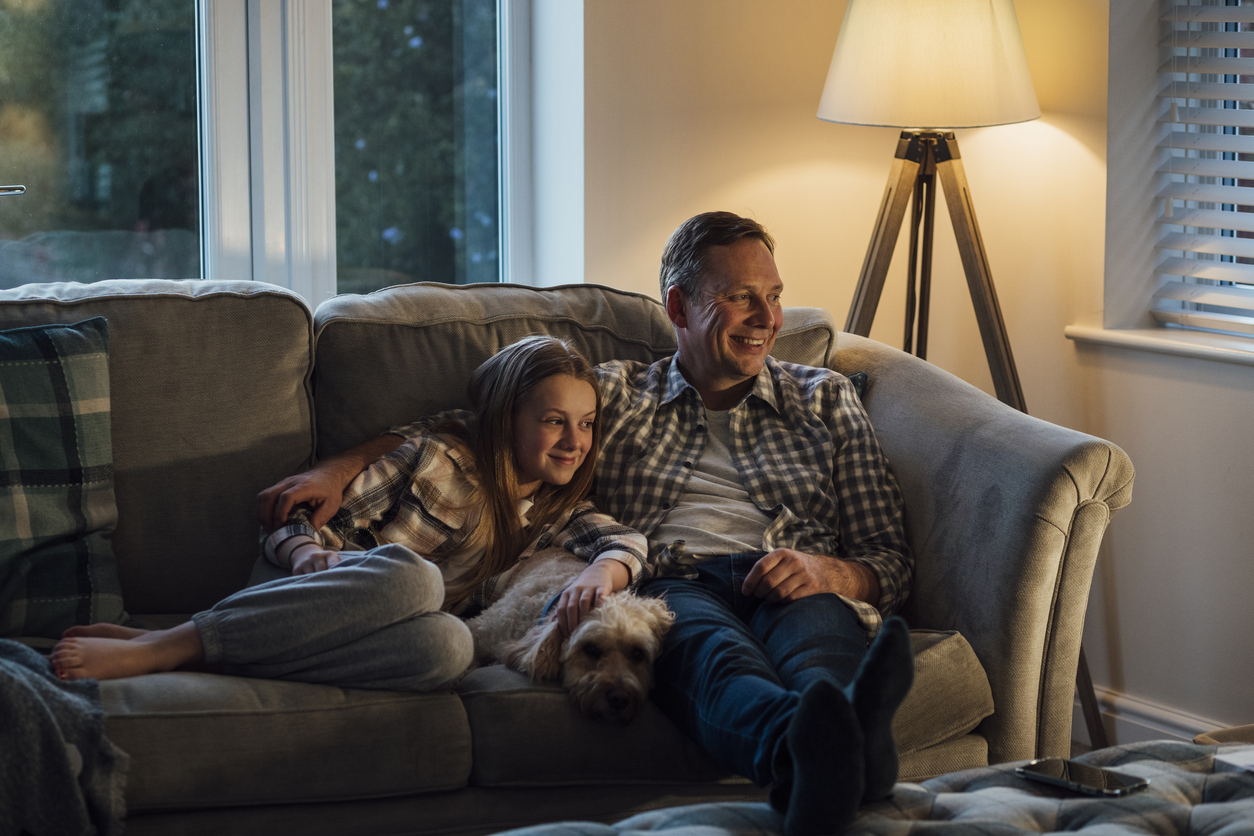 Pappa och dotter sitter i soffa och tittar på tv