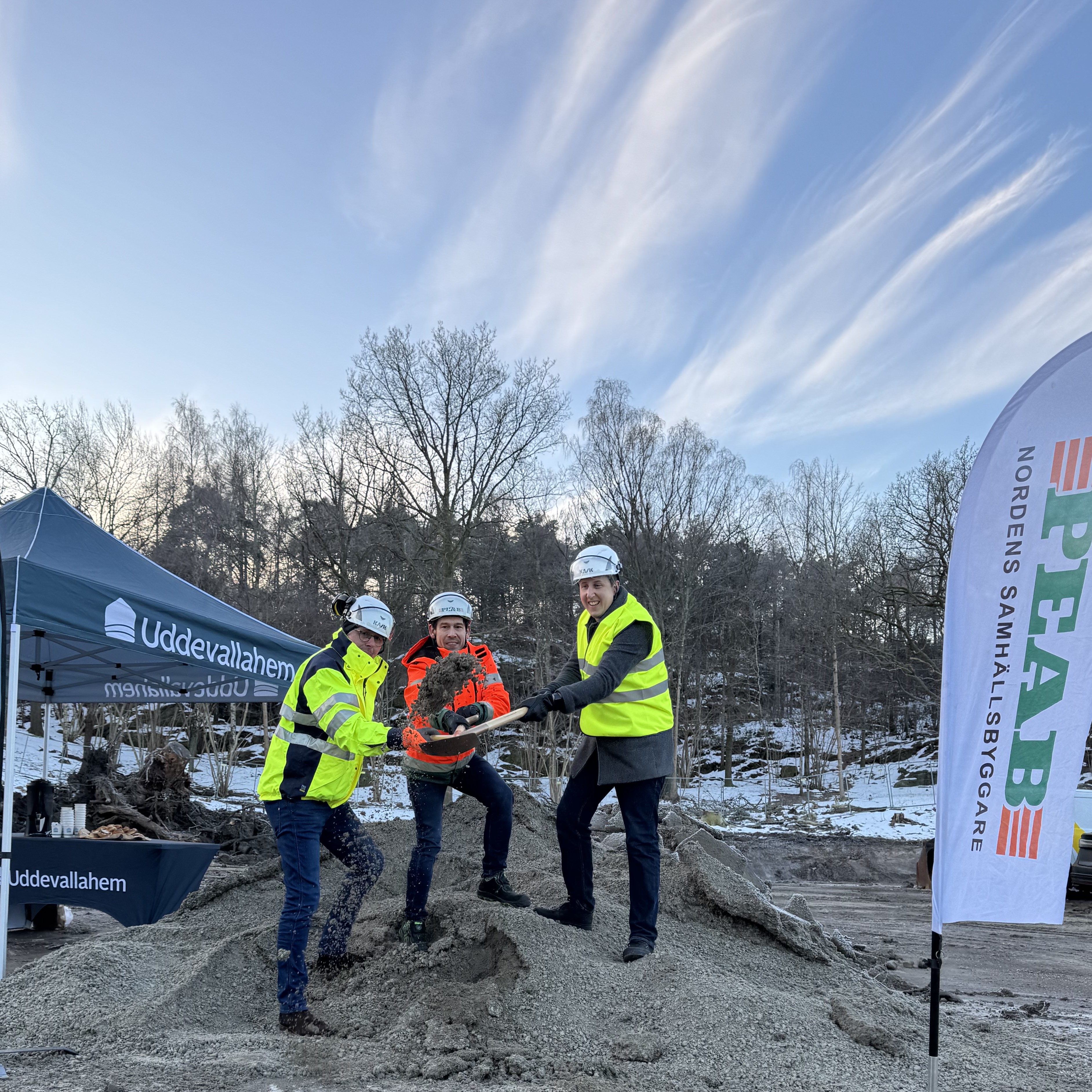 Tre personer i varselkläder och hjälm tar ett gemensamt spadtag